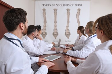 Image of Team of doctors using video projector during conference about scoliosis indoors. Illustrations on projection screen