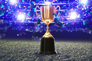 Image of Football championship. Shiny golden trophy cup under falling confetti on illuminated stadium