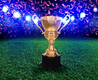 Image of Football championship. Shiny golden trophy cup under falling confetti on illuminated stadium
