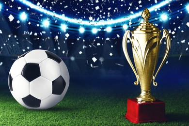 Image of Football championship. Shiny golden trophy cup and soccer ball under falling confetti on stadium