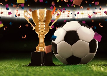 Image of Football championship. Shiny golden trophy cup and soccer ball under falling confetti on stadium