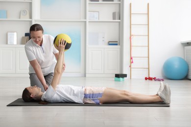 Photo of Doctor and patient exercising with medicine ball in clinic