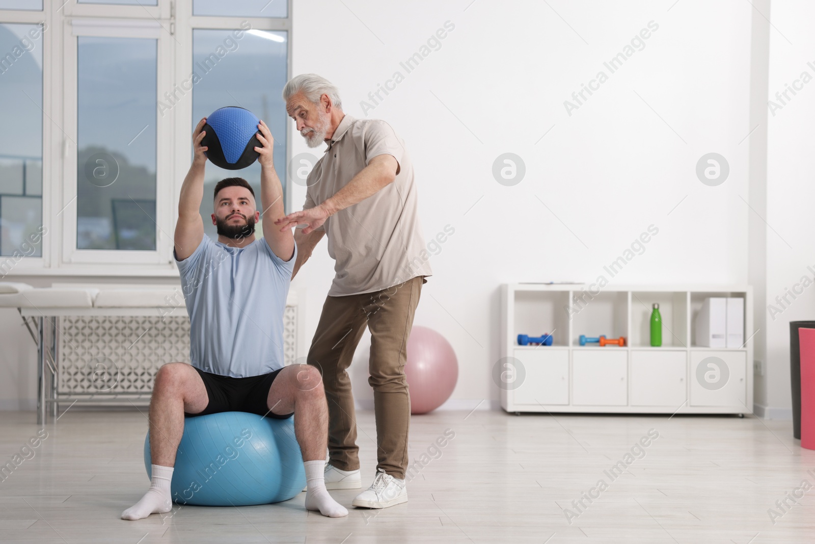 Doctor and patient exercising with medicine ball in clinic, space for text Photo of Doctor and patient exercising with medicine ball in clinic, space for text