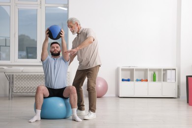 Photo of Doctor and patient exercising with medicine ball in clinic, space for text