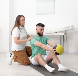 Photo of Doctor and patient exercising with medicine ball in clinic