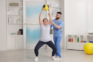Photo of Doctor and patient exercising with medicine ball in clinic