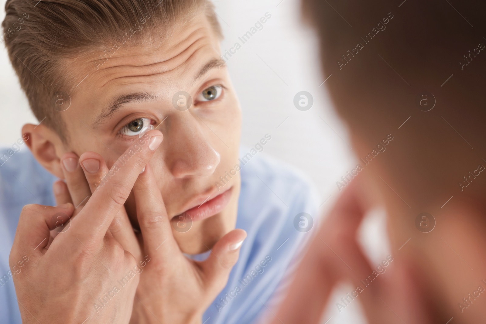 Man putting in contact lens near mirror at home, closeup Photo of Man putting in contact lens near mirror at home, closeup