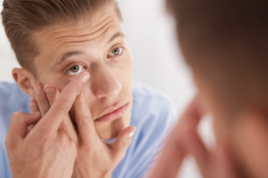 Photo of Man putting in contact lens near mirror at home, closeup