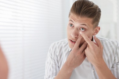 Photo of Man putting in contact lens at home. Space for text
