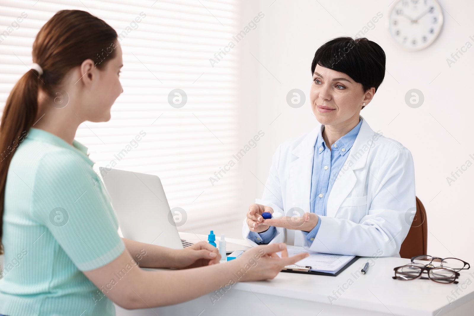 Ophthalmologist giving contact lenses to patient at table in office Photo of Ophthalmologist giving contact lenses to patient at table in office