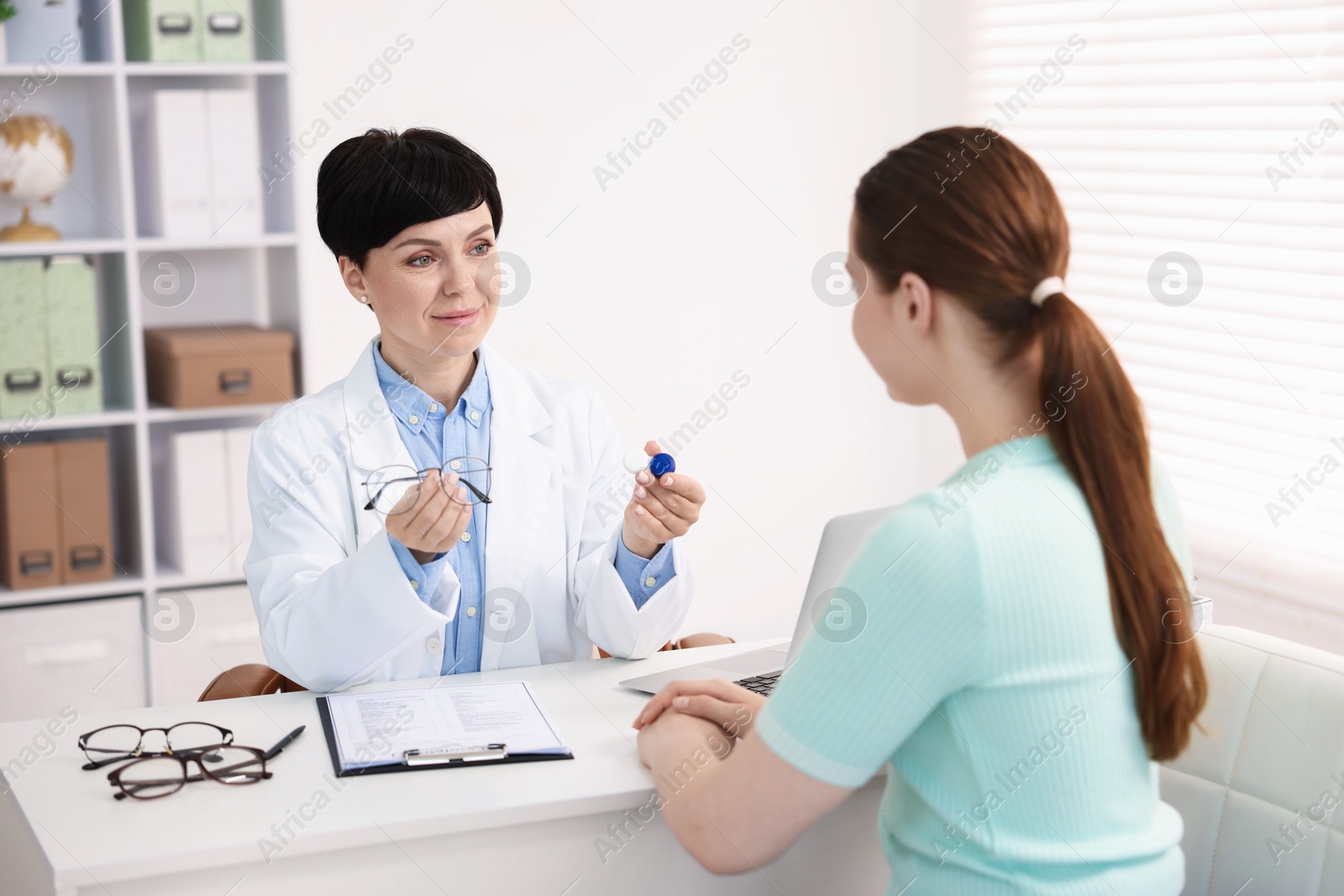 Ophthalmologist giving contact lenses and glasses to patient at table in office Photo of Ophthalmologist giving contact lenses and glasses to patient at table in office