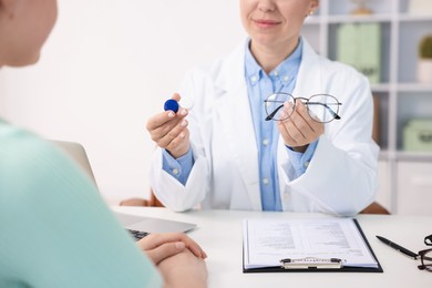 Photo of Ophthalmologist giving contact lenses and glasses to patient at table in office
