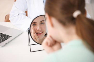Photo of Young woman putting on contact lenses at table near mirror in ophthalmologist office, selective focus