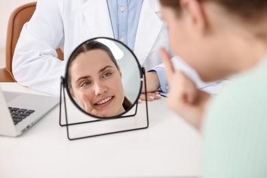 Photo of Young woman putting on contact lenses at table near mirror in ophthalmologist office, selective focus