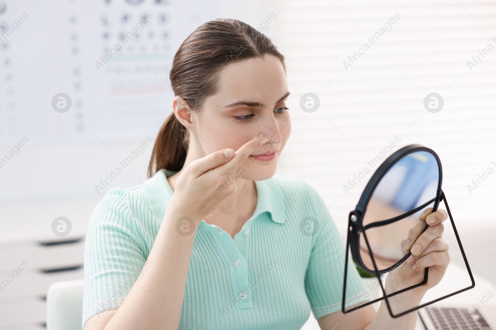 Young woman putting on contact lenses near mirror in ophthalmologist office Photo of Young woman putting on contact lenses near mirror in ophthalmologist office