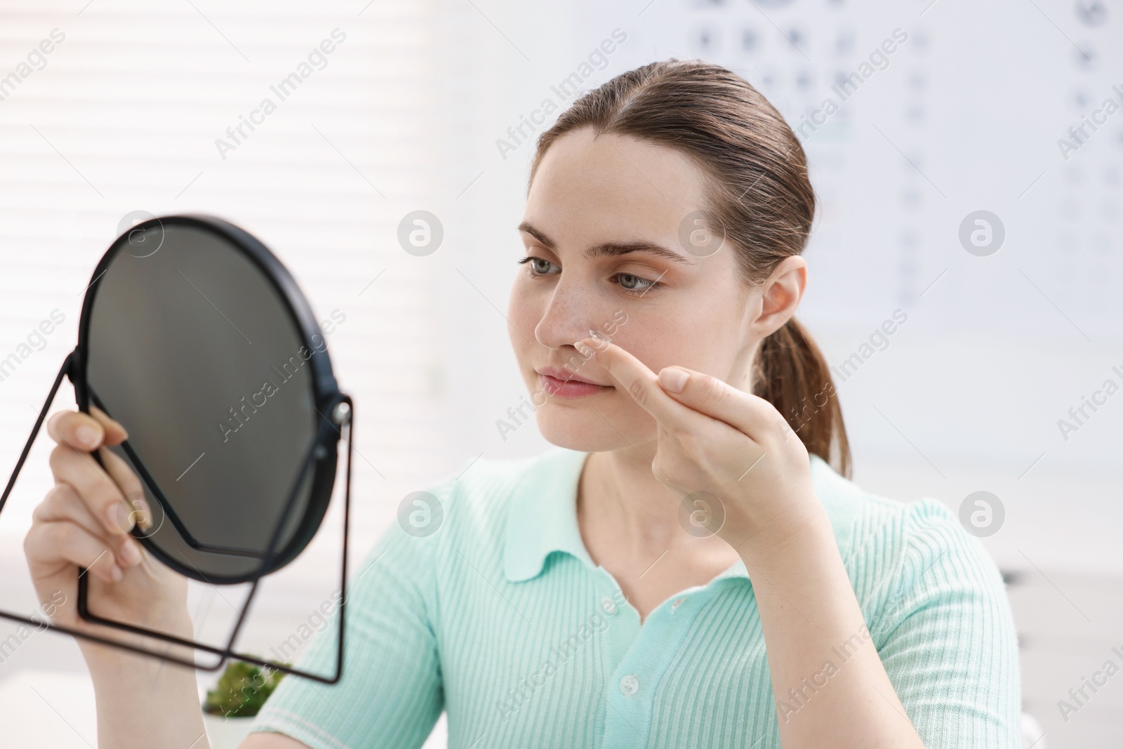 Young woman putting on contact lenses near mirror in ophthalmologist office Photo of Young woman putting on contact lenses near mirror in ophthalmologist office