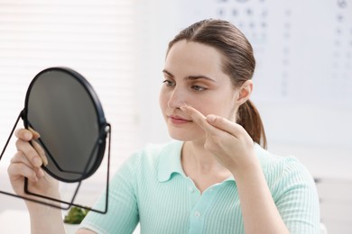 Photo of Young woman putting on contact lenses near mirror in ophthalmologist office