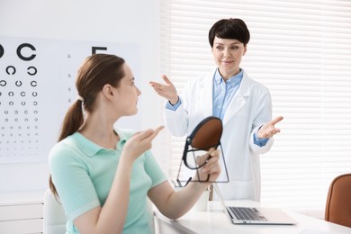 Photo of Ophthalmologist teaching patient to use contact lenses at table in office