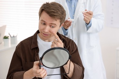 Photo of Young man putting on contact lenses near mirror in ophthalmologist office