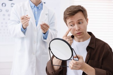 Photo of Young man putting on contact lenses near mirror in ophthalmologist office