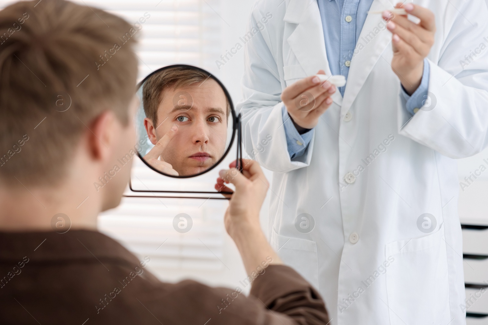 Young man putting on contact lenses near mirror in ophthalmologist office, selective focus Photo of Young man putting on contact lenses near mirror in ophthalmologist office, selective focus
