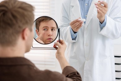 Photo of Young man putting on contact lenses near mirror in ophthalmologist office, selective focus