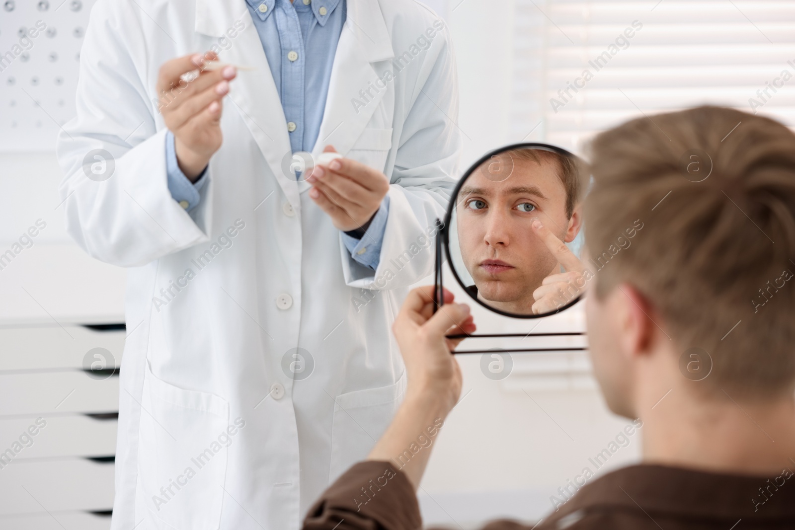 Young man putting on contact lenses near mirror in ophthalmologist office, selective focus Photo of Young man putting on contact lenses near mirror in ophthalmologist office, selective focus