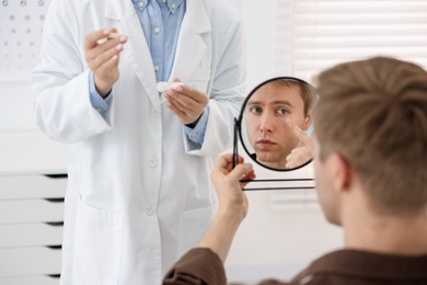 Photo of Young man putting on contact lenses near mirror in ophthalmologist office, selective focus