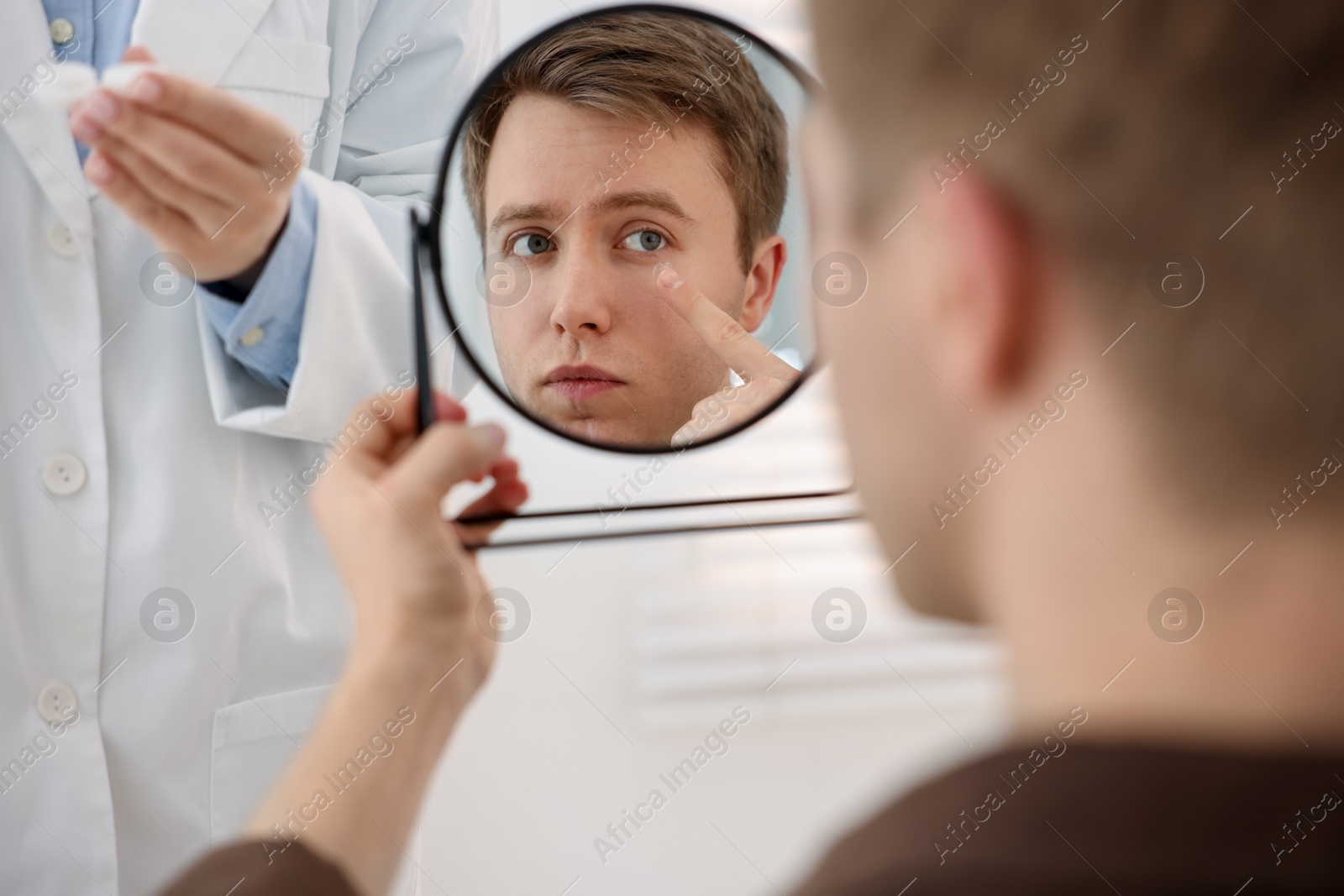 Young man putting on contact lenses near mirror in ophthalmologist office, selective focus Photo of Young man putting on contact lenses near mirror in ophthalmologist office, selective focus