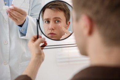 Photo of Young man putting on contact lenses near mirror in ophthalmologist office, selective focus