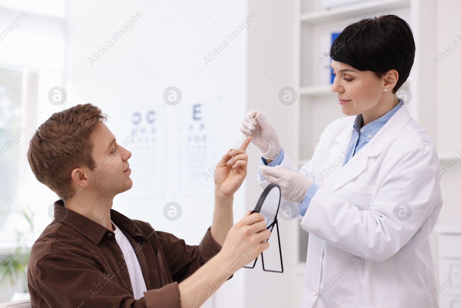 Young man putting on contact lenses near mirror in ophthalmologist office Photo of Young man putting on contact lenses near mirror in ophthalmologist office