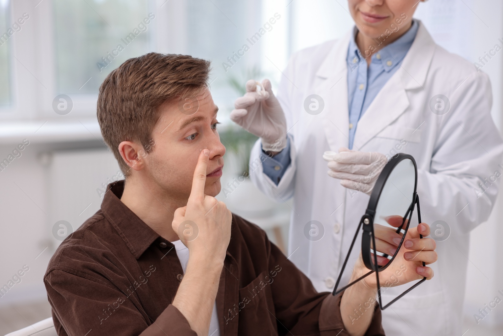 Young man putting on contact lenses near mirror in ophthalmologist office Photo of Young man putting on contact lenses near mirror in ophthalmologist office