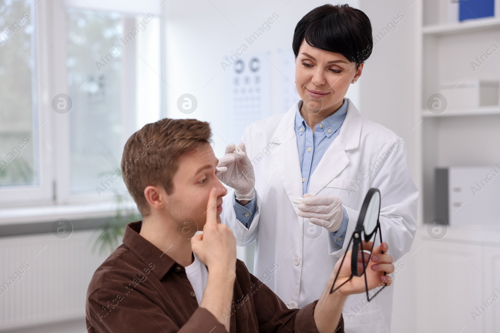 Young man putting on contact lenses near mirror in ophthalmologist office Photo of Young man putting on contact lenses near mirror in ophthalmologist office