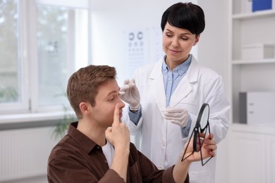 Photo of Young man putting on contact lenses near mirror in ophthalmologist office