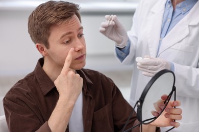 Photo of Young man putting on contact lenses near mirror in ophthalmologist office