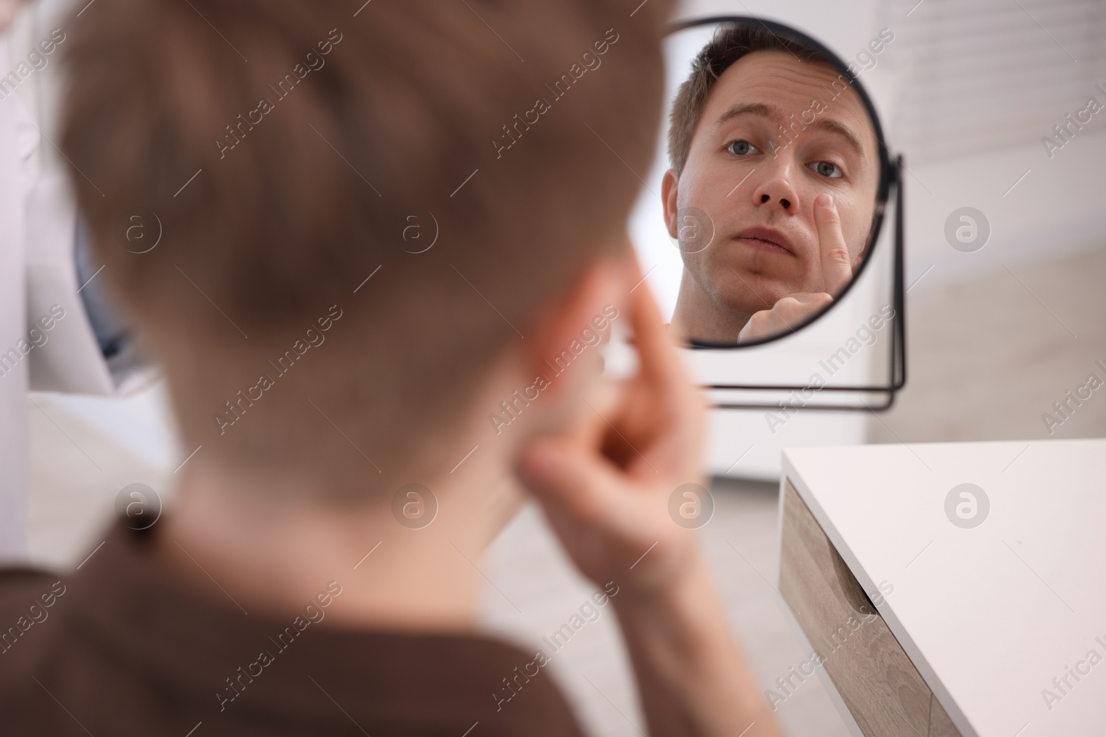 Young man putting on contact lenses near mirror in ophthalmologist office, selective focus Photo of Young man putting on contact lenses near mirror in ophthalmologist office, selective focus