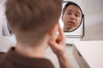 Photo of Young man putting on contact lenses near mirror in ophthalmologist office, selective focus