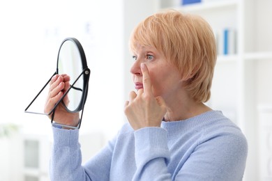 Photo of Senior woman putting on contact lenses near mirror in ophthalmologist office