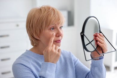 Photo of Senior woman putting on contact lenses near mirror in ophthalmologist office