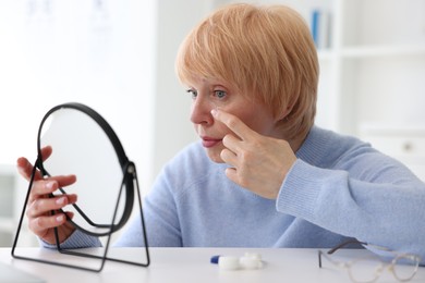 Photo of Senior woman putting on contact lenses at table near mirror in ophthalmologist office