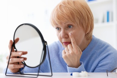 Photo of Senior woman putting on contact lenses at table near mirror in ophthalmologist office
