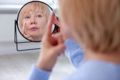 Photo of Senior woman putting on contact lenses near mirror in ophthalmologist office, selective focus