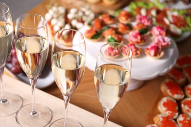Photo of Buffet menu. Glasses of sparkling wine and tasty appetizers on table, closeup