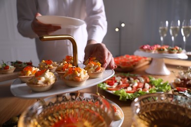 Photo of Buffet menu. Woman taking tasty tartlet from table, closeup