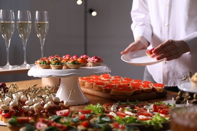 Photo of Buffet menu. Woman taking tasty tartlet from table, closeup