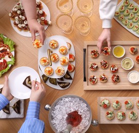 Photo of Buffet menu. People taking tasty appetizers from wooden table, top view