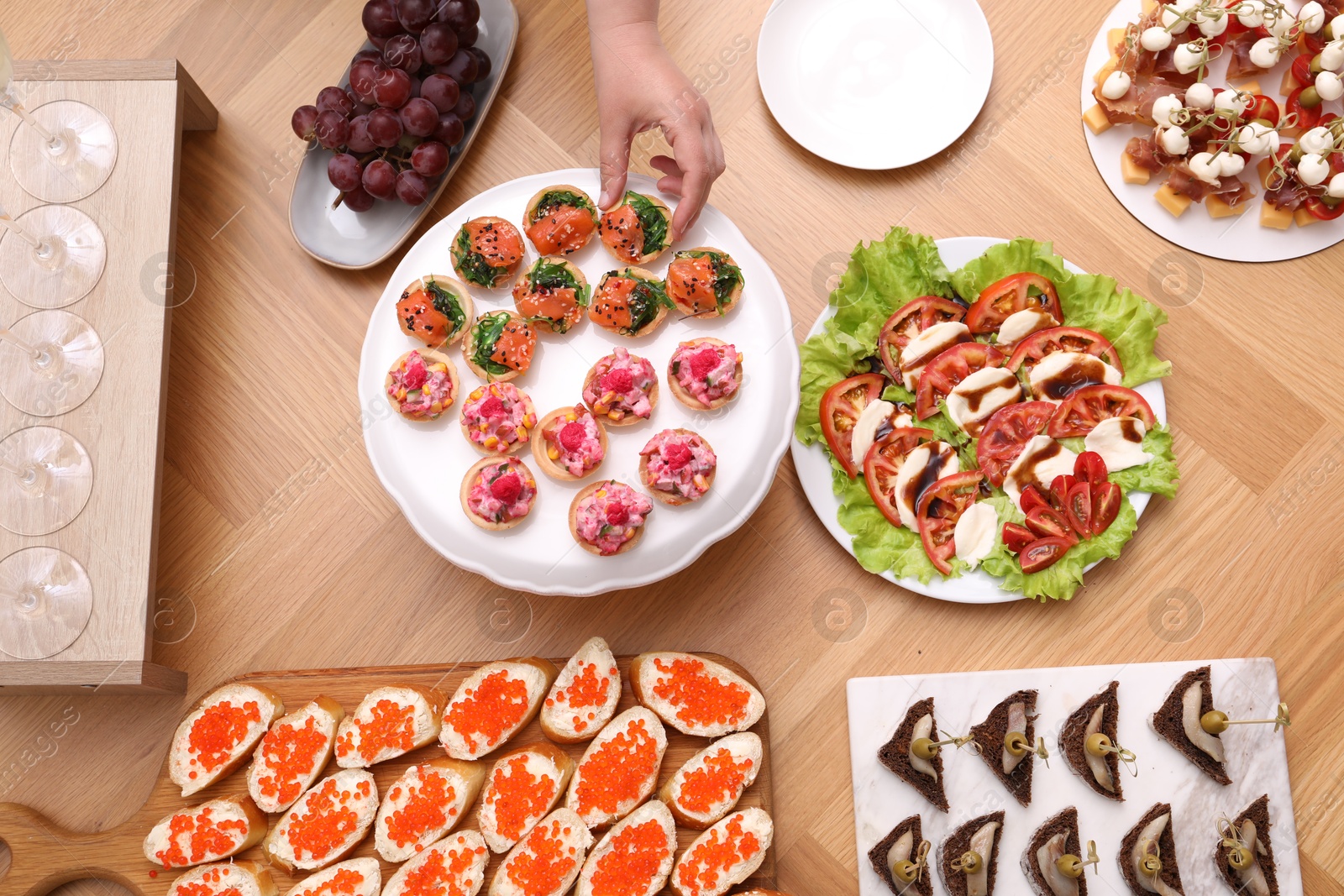 Buffet menu. Woman taking tasty tartlet from wooden table, top view Photo of Buffet menu. Woman taking tasty tartlet from wooden table, top view