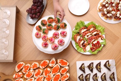 Photo of Buffet menu. Woman taking tasty tartlet from wooden table, top view
