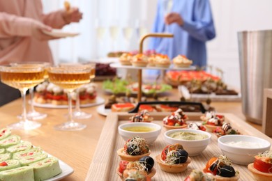 Photo of Different tasty appetizers on table and women enjoying buffet, selective focus