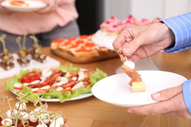 Photo of Buffet menu. Woman taking tasty canape from table, closeup
